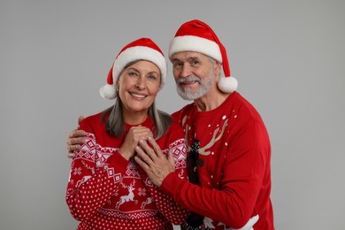 Photo of Happy senior couple in Christmas sweaters and Santa hats on grey background
