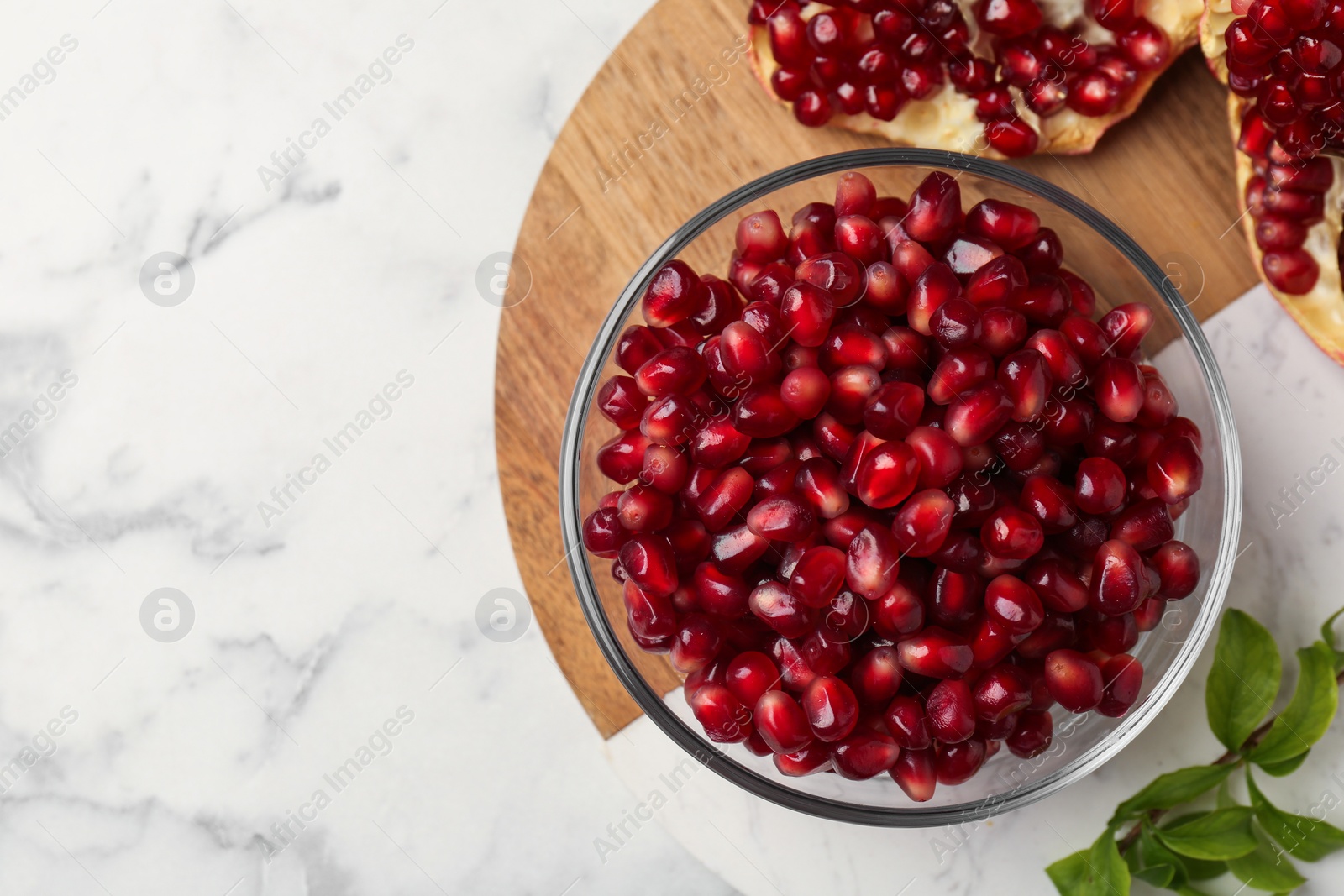 Photo of Ripe juicy pomegranate grains and green leaves on white marble table, top view. Space for text