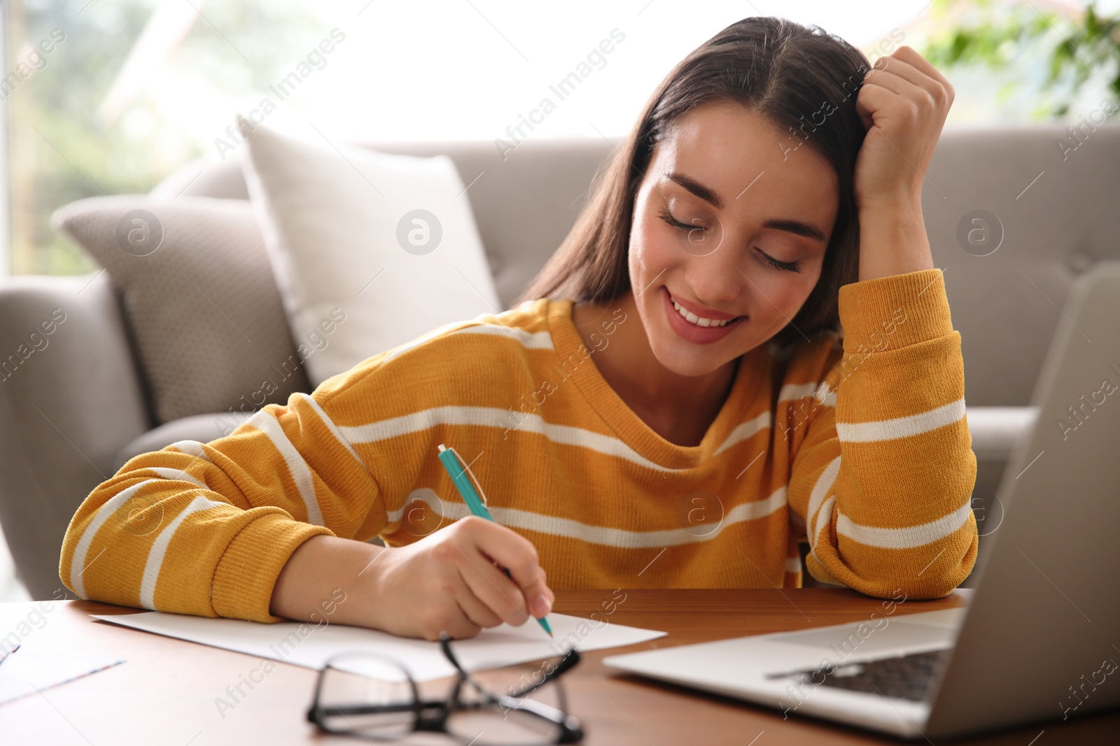 Photo of Woman writing letter at wooden table in room