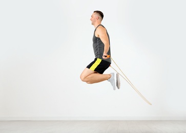 Photo of Young sportive man training with jump rope in light room