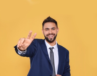 Photo of Happy young businessman showing victory gesture on color background