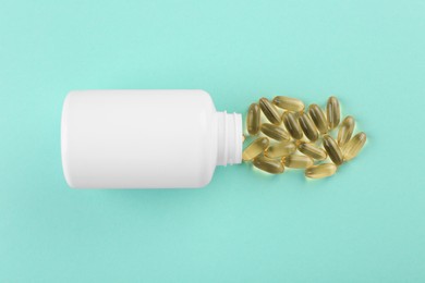 Bottle and vitamin capsules on turquoise background, top view