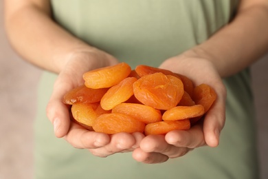 Photo of Woman holding handful of dried apricots on color background, closeup. Healthy fruit