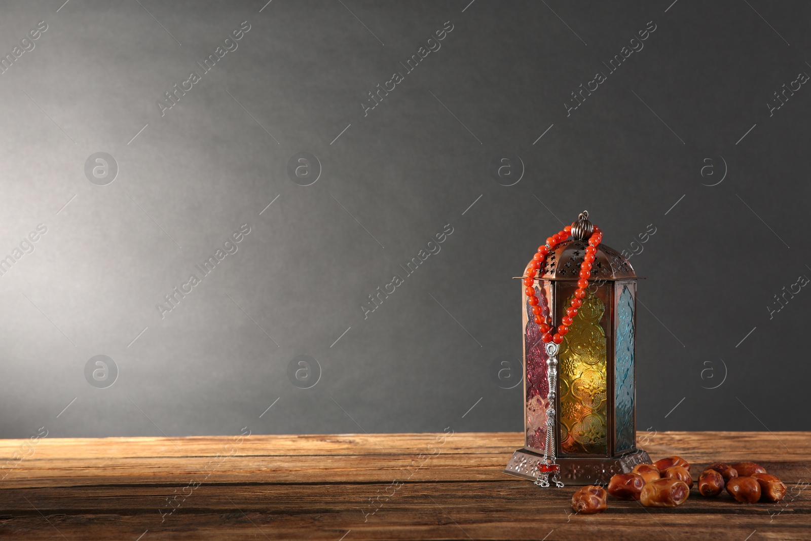 Photo of Muslim lamp, dates and prayer beads on wooden table against dark background. Space for text