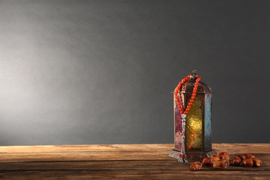 Photo of Muslim lamp, dates and prayer beads on wooden table against dark background. Space for text