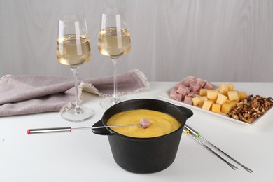 Fondue with tasty melted cheese, forks, different products and aromatic wine in glasses on white table