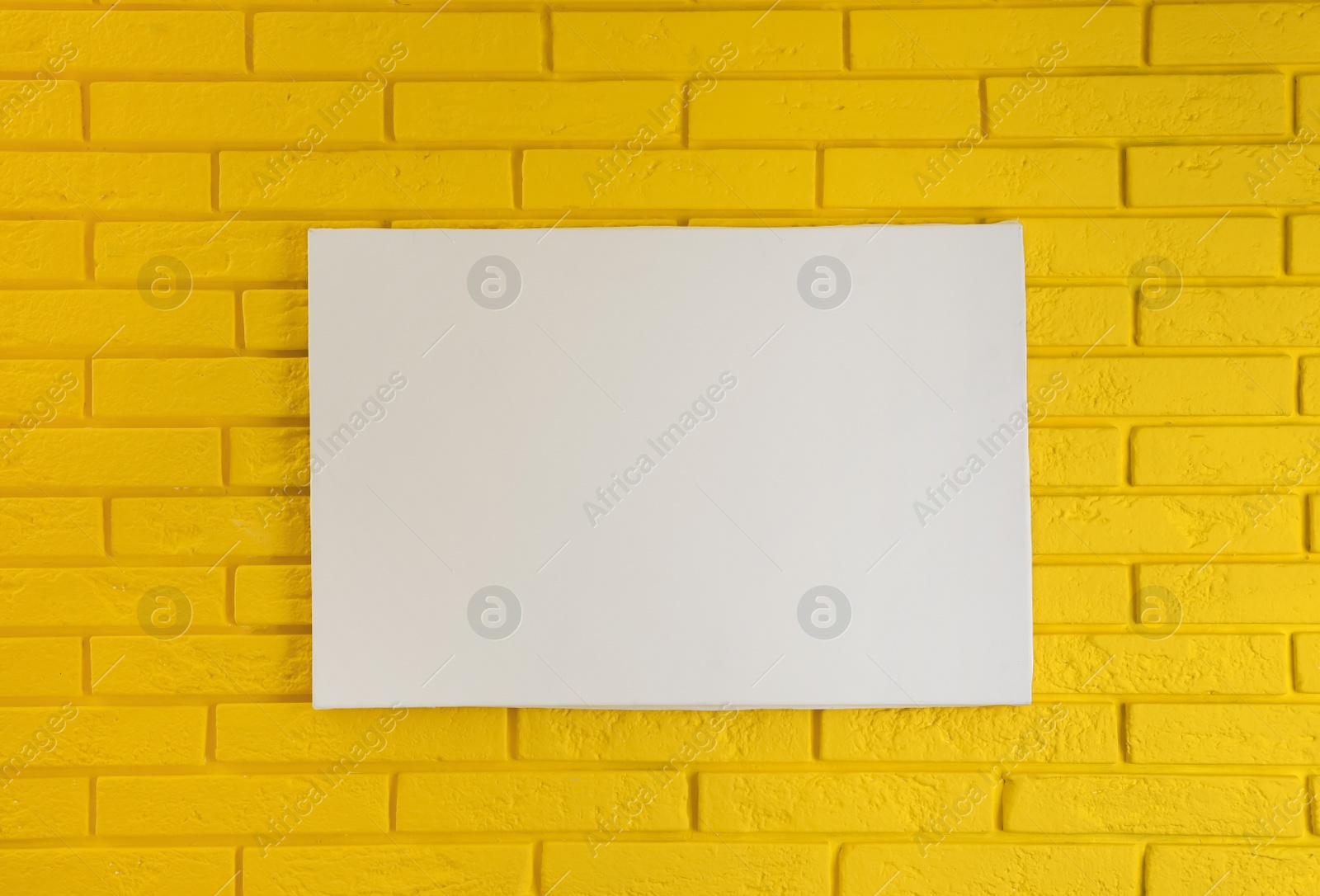 Photo of Blank canvas on yellow brick wall. Space for design