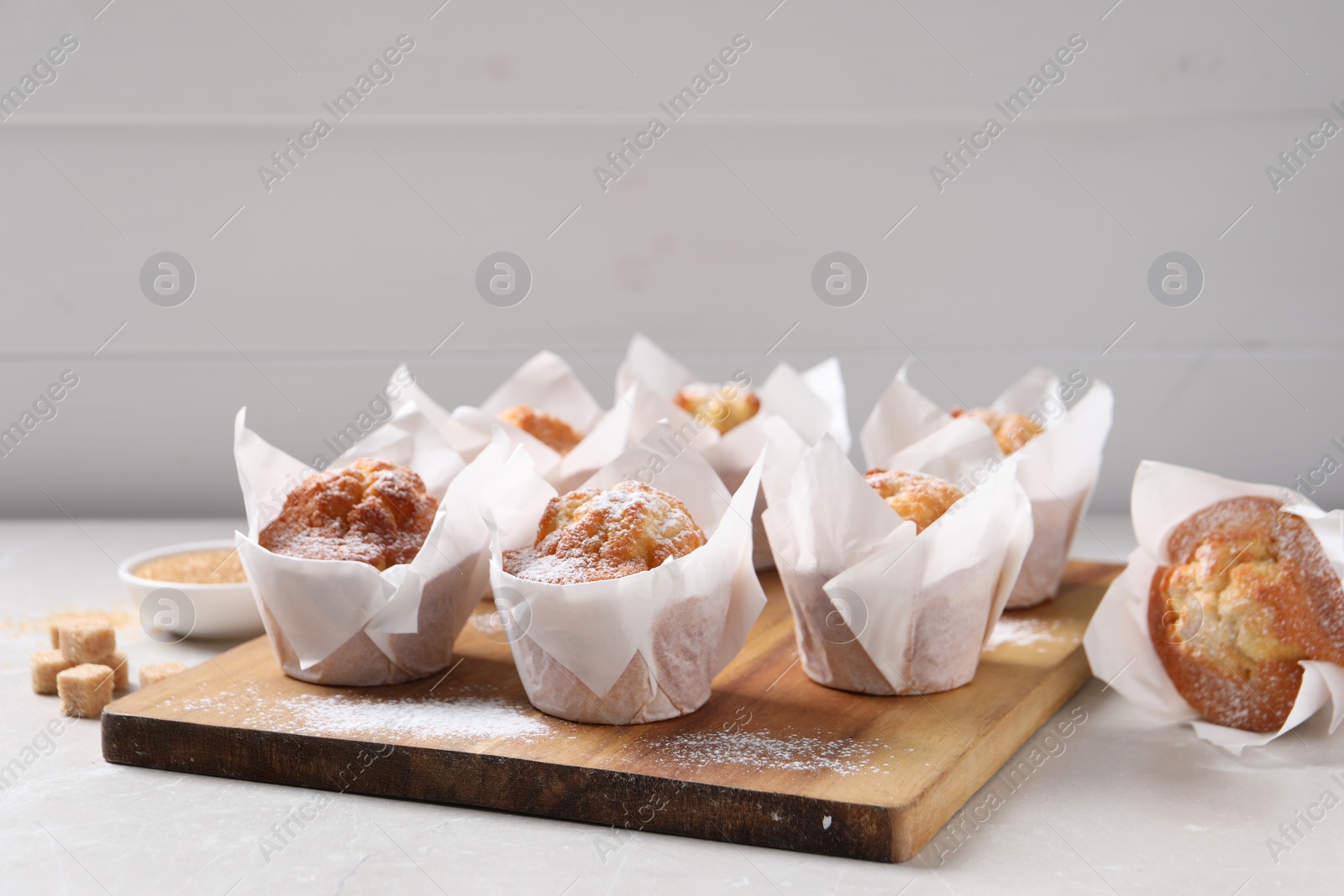 Photo of Delicious muffins with powdered sugar on light table