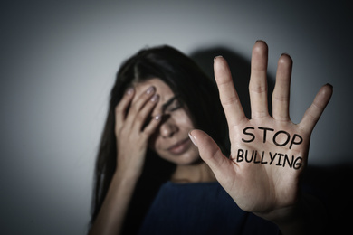Image of Crying teen girl showing palm with message STOP BULLYING near white wall, focus on hand