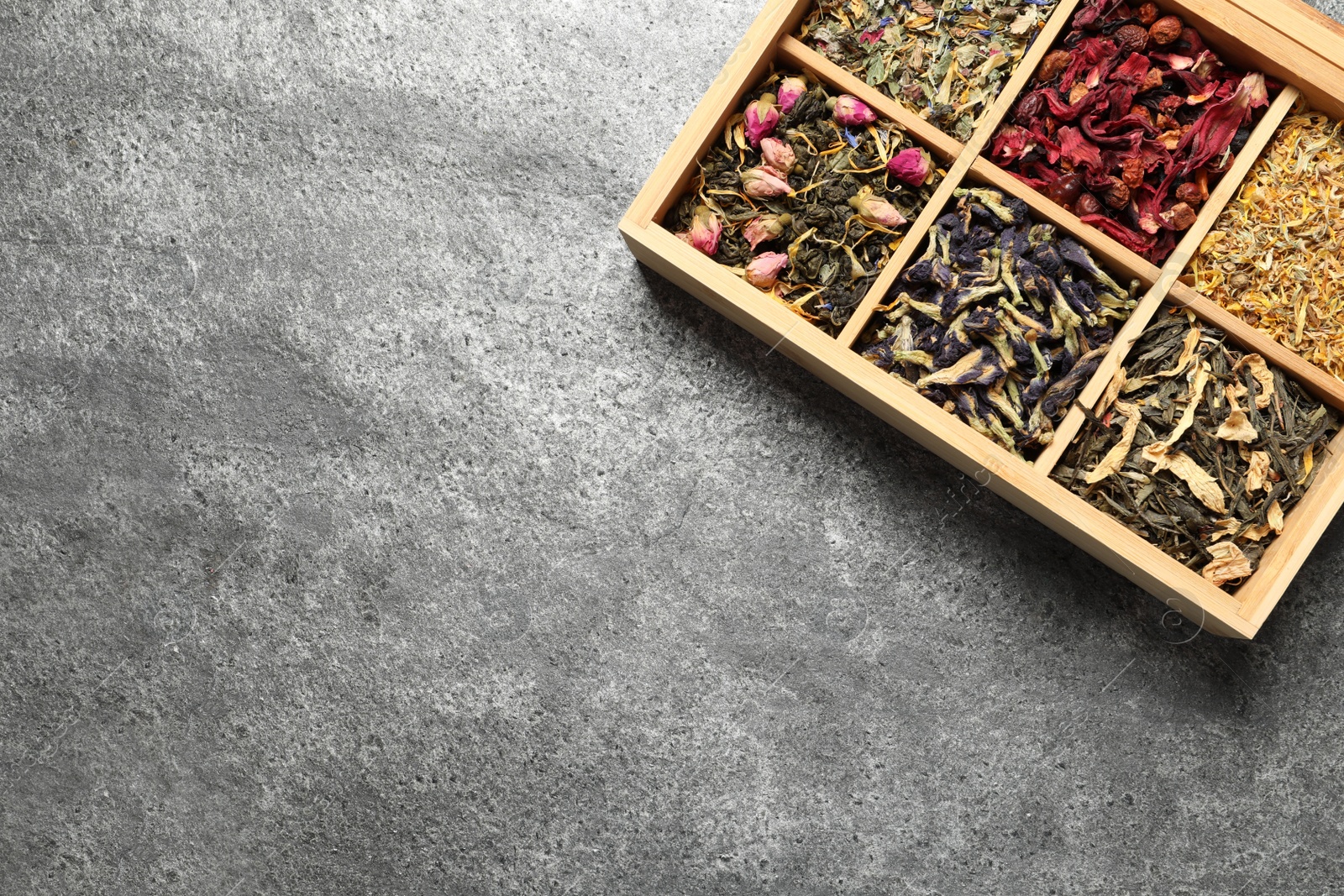 Photo of Different dry herbal teas in wooden box on grey table, top view. Space for text