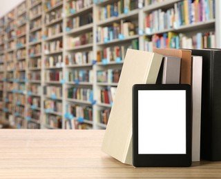 Image of Hardcover books and modern e-book on wooden table in library. Space for text