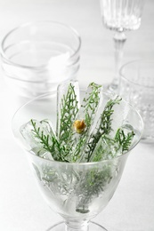 Glass of ice cubes with cedar branches on light table, closeup