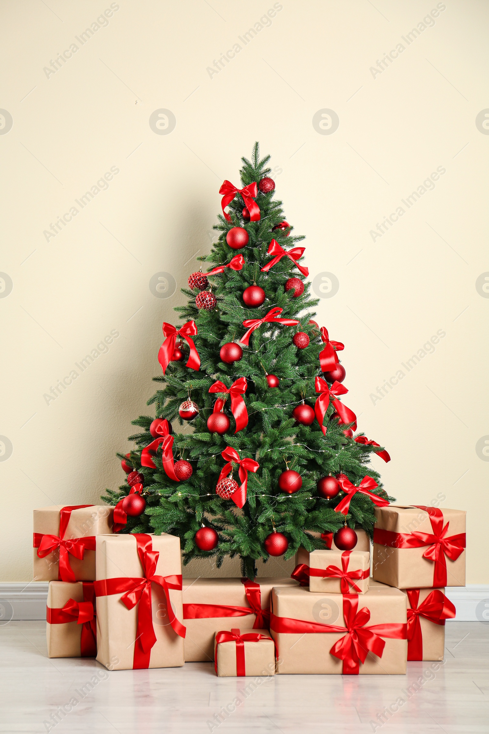 Photo of Decorated Christmas tree and gift boxes near beige wall