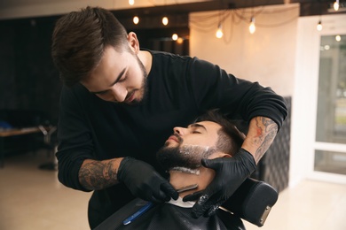 Photo of Professional hairdresser shaving client with straight razor in barbershop