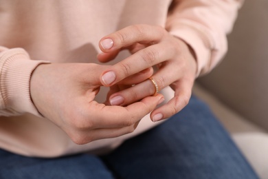 Photo of Woman taking off wedding ring on sofa, closeup. Divorce concept