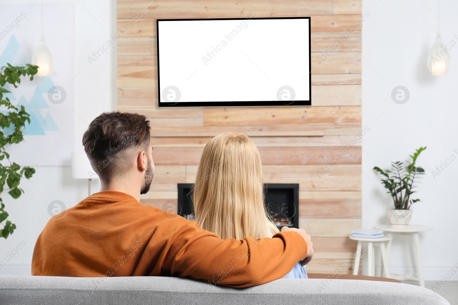 Photo of Couple watching TV on sofa in living room with decorative fireplace