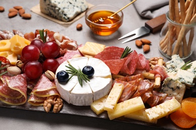 Photo of Wooden board with different appetizers on grey table, closeup