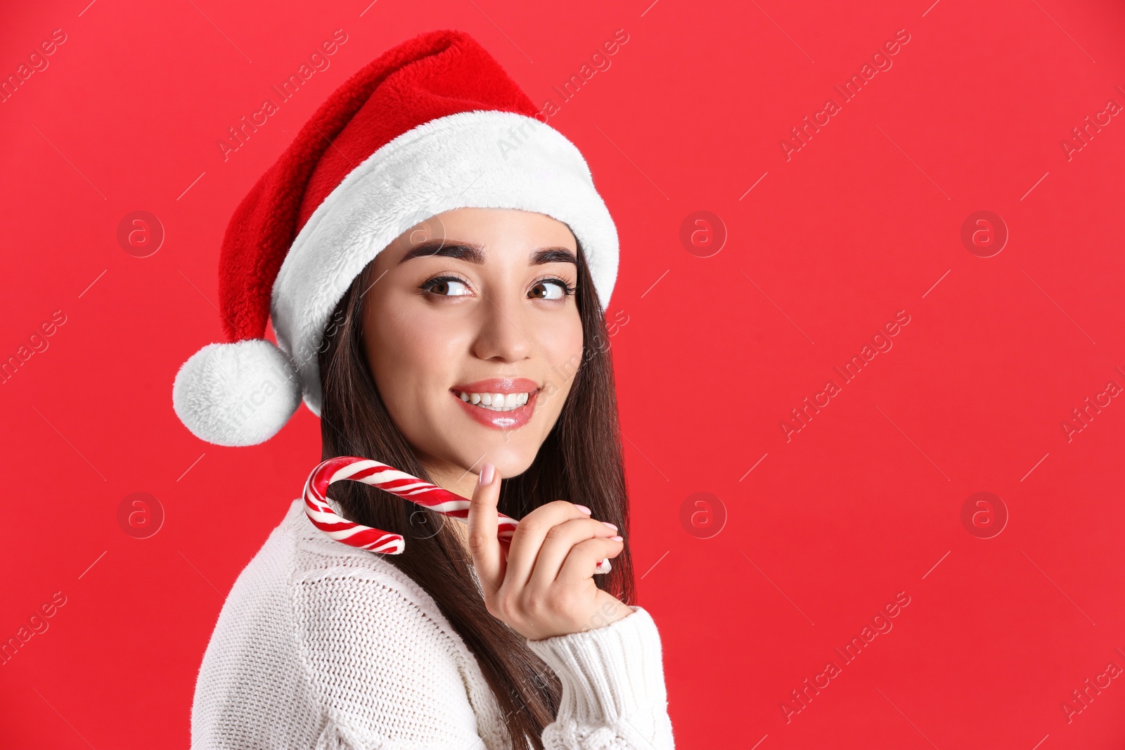 Photo of Beautiful woman in Santa Claus hat holding candy cane on red background. Space for text