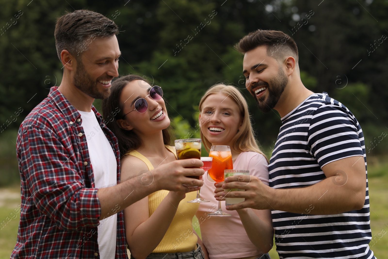 Photo of Happy friends clinking glasses with cocktails outdoors