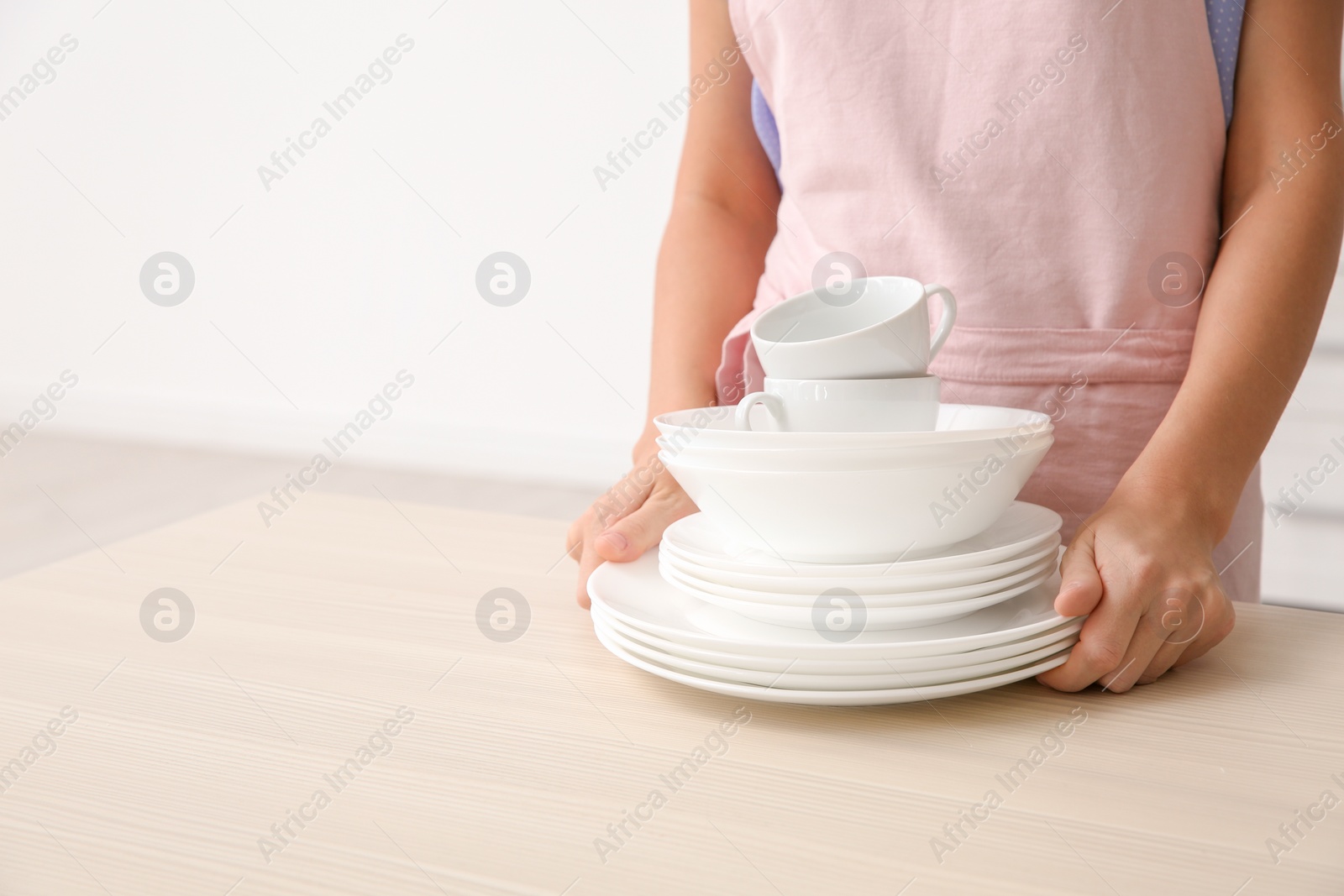 Photo of Woman with clean dishes and cups in kitchen, closeup. Space for text