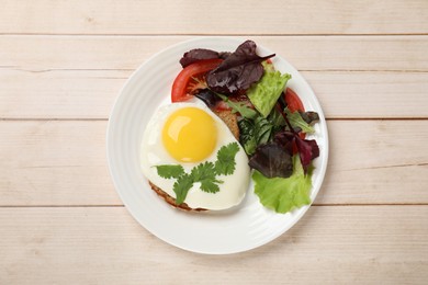 Photo of Plate with tasty fried egg, slice of bread and salad on light wooden table, top view
