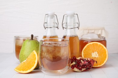 Photo of Tasty kombucha with ice cubes and fresh fruits on white tiled table