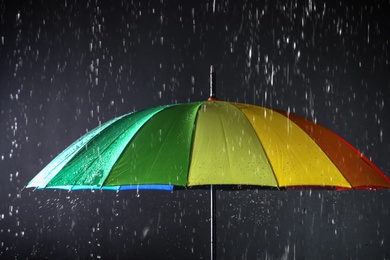 Photo of Bright umbrella under rain on dark background