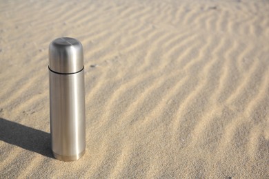 Photo of Metallic thermos with hot drink on sand, space for text