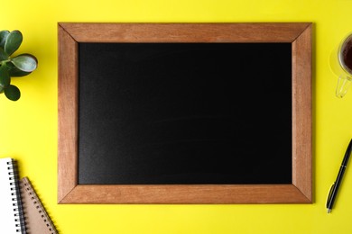 Photo of Clean small chalkboard, plant and stationery on yellow background, flat lay
