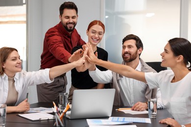 Photo of Team of employees joining hands in office