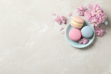 Photo of Delicious colorful macarons and pink flowers on light grey table, flat lay. Space for text