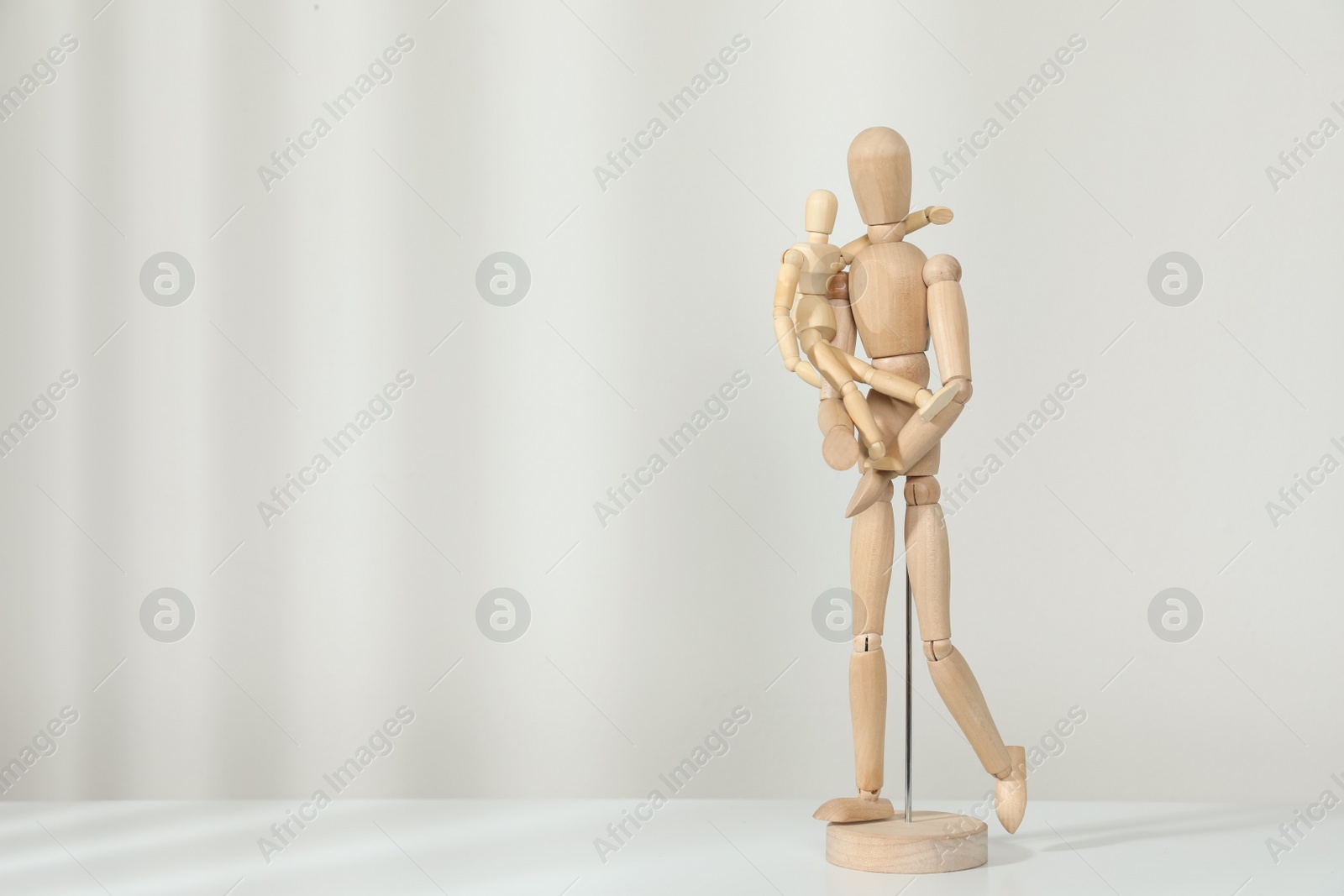 Photo of Wooden mannequins of parent with child on white table against light background, space for text. Family Day