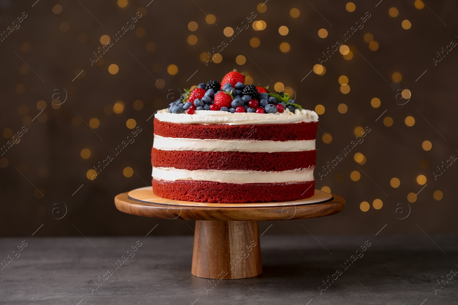 Photo of Stand with delicious homemade red velvet cake against blurred lights