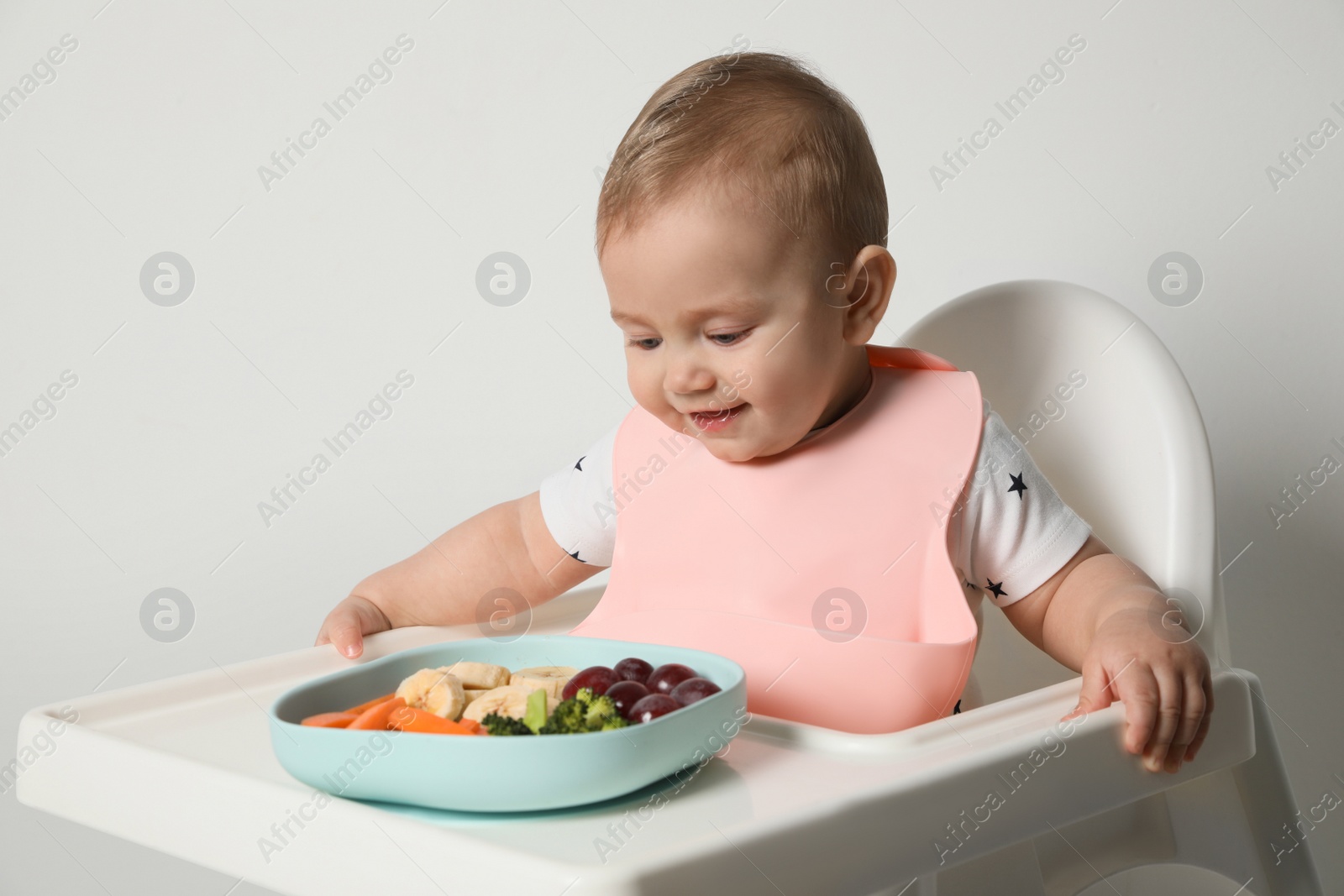 Photo of Cute little baby wearing bib while eating on white background