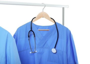 Photo of Light blue medical uniforms and stethoscope on rack against white background