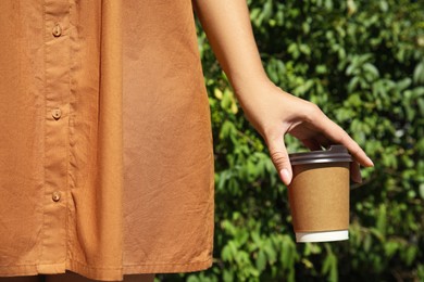 Woman holding takeaway cardboard coffee cup with plastic lid outdoors, closeup