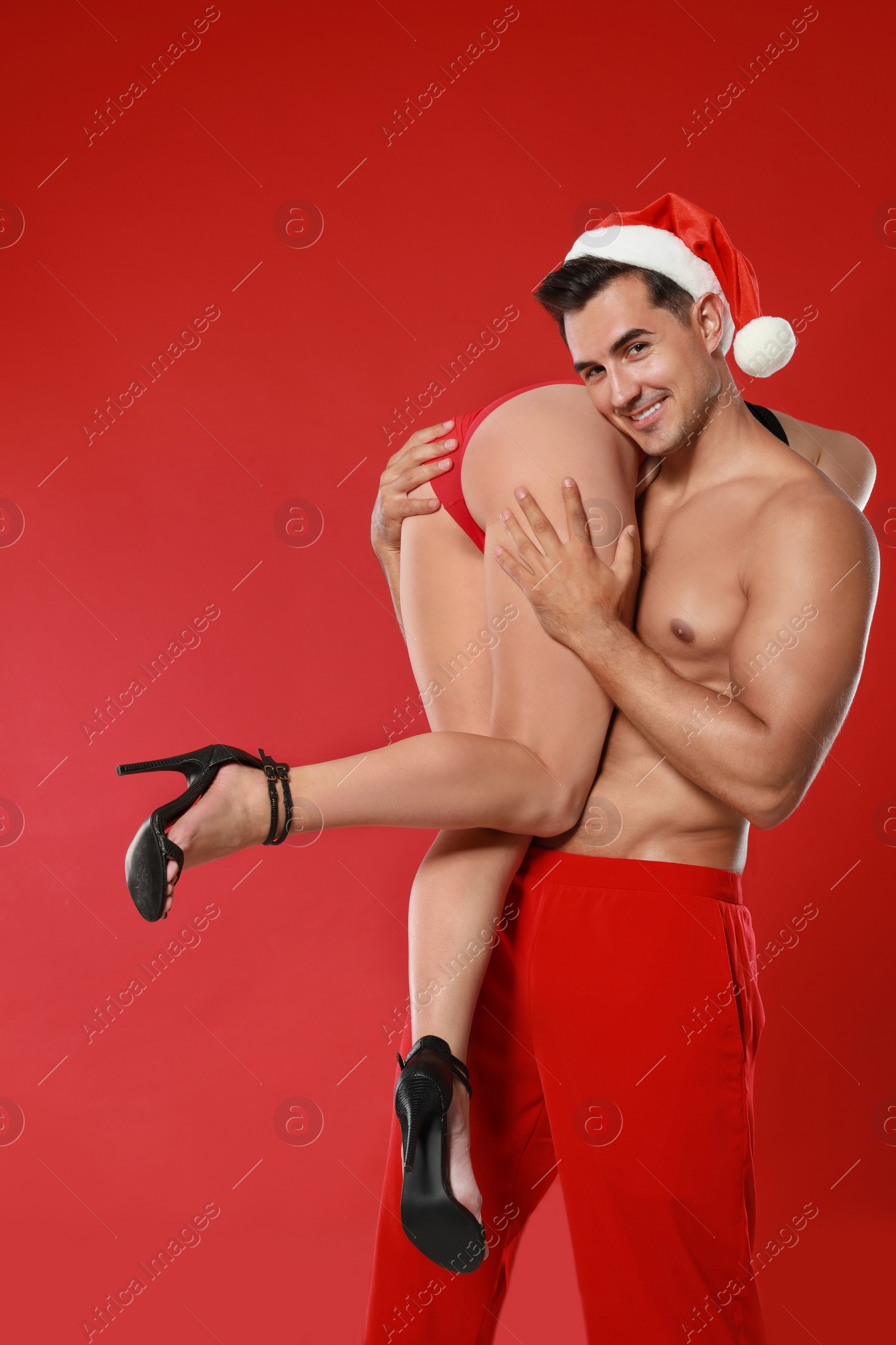 Photo of Attractive young Santa Claus with sexy woman on red background