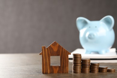 House model, stacked coins and piggy bank on wooden table, selective focus. Space for text