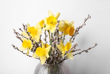 Bouquet of beautiful yellow daffodils and willow twigs in vase on white background