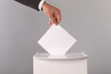 Man putting his vote into ballot box on light grey background, closeup