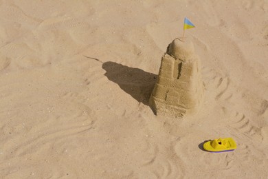 Photo of Beautiful sand castle with small Ukrainian flag and toy boat on beach, space for text