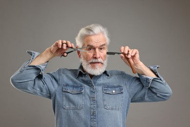 Photo of Senior man with mustache holding blade and scissors on grey background
