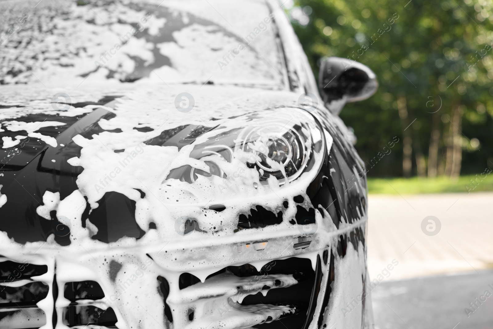 Photo of Auto covered with cleaning foam at outdoor car wash, closeup