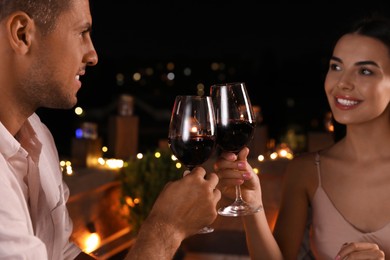 Photo of Romantic couple with glasses of red wine on cafe terrace at night, closeup