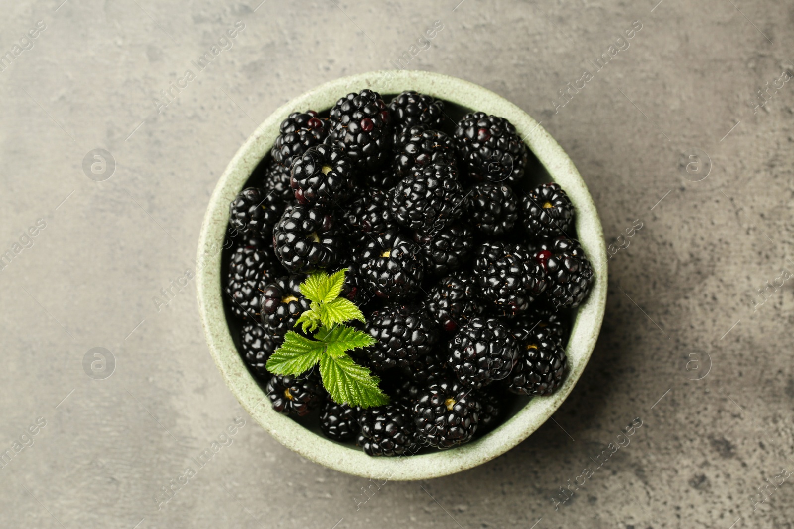 Photo of Bowl with fresh ripe blackberries on grey table, top view