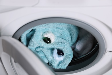 Photo of Laundry detergent capsules and towels in washing machine drum, closeup view