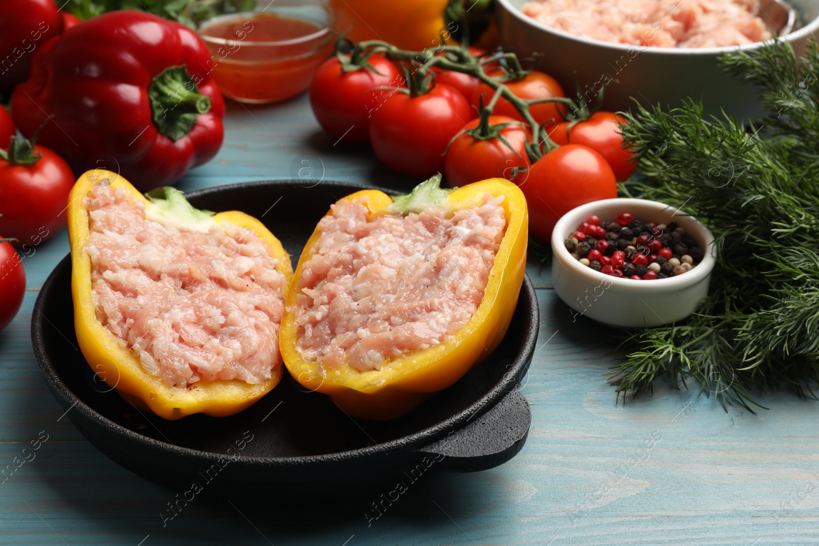 Photo of Raw stuffed peppers with ground meat and ingredients on light blue wooden table