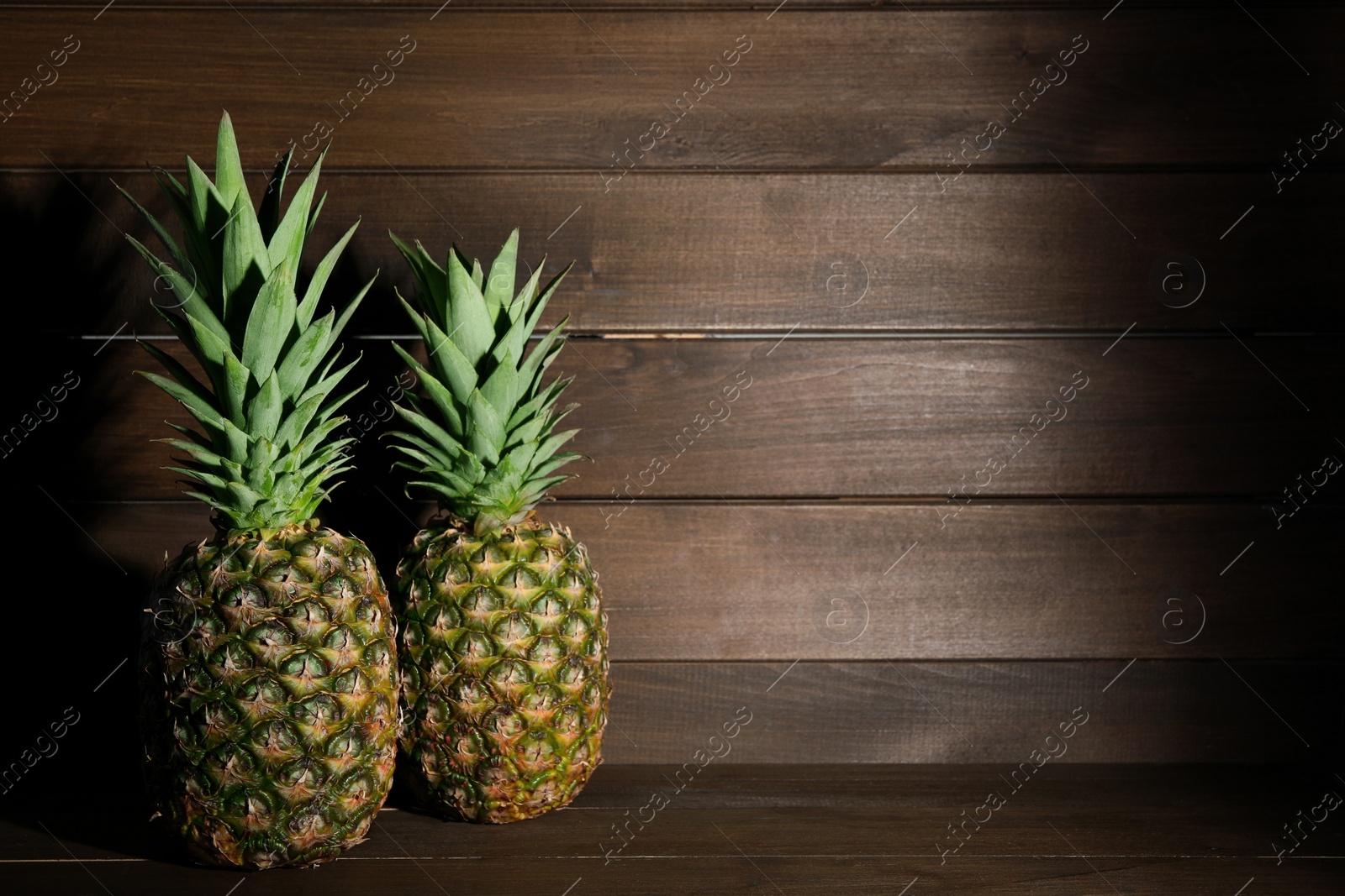Photo of Whole ripe pineapples on wooden table, space for text