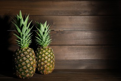 Photo of Whole ripe pineapples on wooden table, space for text