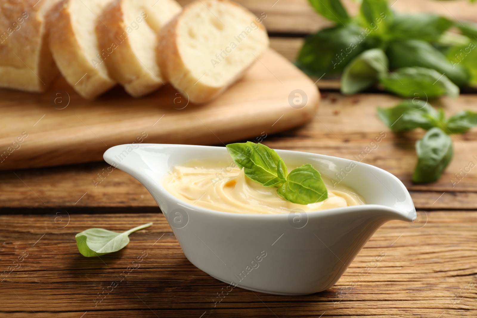 Photo of Tasty sauce with basil leaves in gravy boat on wooden table